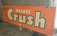 Full view of Orange Crush tin sign with bottle in front