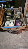 Box filled with assorted picture frames and some framed photos