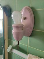 Pink porcelain wall sconce mounted on green tile wall with bulb installed