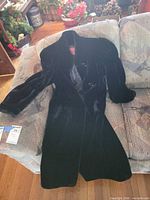 Full view of black faux-fur velvet coat laid on sofa