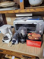 Lot overview showing toaster oven, coffeemaker, handheld vacuum, Cuisinart processor, boxed garlic baker