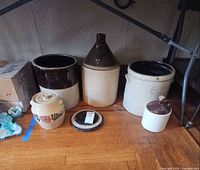 All crocks, jugs, cookie jar and lid grouped under table