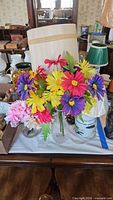 Table lamp base with shade, multicolour daisy arrangement in vase, partial view of peony arrangement