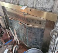 Front view of brass-tone fireplace door assembly installed in stone fireplace