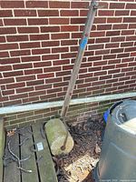 Full view of concrete lawn roller with wooden handle leaning against brick wall