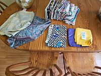 overall view showing stacks of quilting cotton, paisley satin pieces, novelty prints and solids on dining table