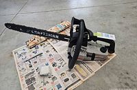 Left side view of Craftsman chainsaw on newspaper with spare chain and hardware