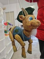 Front angled view of wooden goat marionette suspended by strings