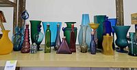 Full shelf view of assorted coloured glass vases, bottles and art glass pieces