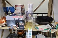 Overall shelf view with boxed pasta machine, meat mincer, food processor parts, goblets, cruet, copper mold, ceramic dishes