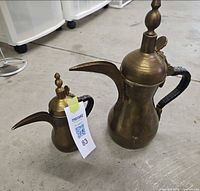 Front view of both brass dallah pots showing size difference and overall form