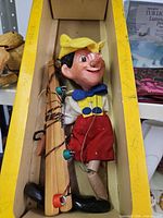 Pinocchio marionette inside yellow Pelham Puppets box with control bar