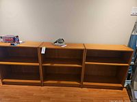 Front view of three identical light brown veneer bookcases side by side