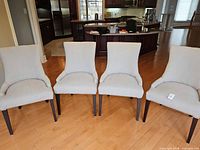 Front view of four beige upholstered Parsons chairs with dark wood legs