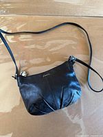 Front view showing black leather Coach purse with pleated bottom and gold logo