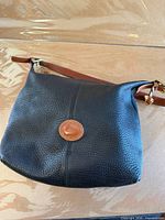 Front of black Dooney & Bourke pebbled leather bag with logo patch and brown strap
