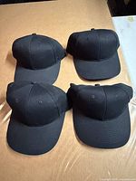 Four black baseball caps displayed top view