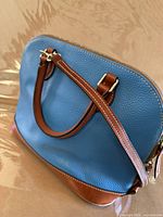 Angled view of blue leather handbag showing handles, trim and side profile