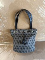 Front view of gray DB monogram tote with black straps and tassel