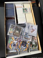 Open box showing numerous trading cards, sleeved cards on left, large stack of loose cards center, modern baseball cards of Clayton Kershaw and Gerrit Cole in foreground, one round Topps coin insert