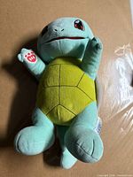 Front view of Squirtle Build-A-Bear plush showing yellow belly, red eyes, left hand paw logo
