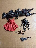 Overview of figure, vehicle, cape, missiles, weapons on cardboard