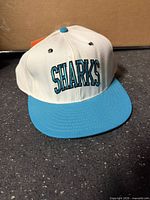 Front view of white cap with teal brim and "SHARKS" embroidery