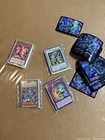 Overview of five Yu-Gi-Oh cards in toploaders and stack of holographic Blue-Eyes sleeves