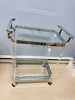 Full view of bar cart showing acrylic frame, chrome trim, top glass shelf, casters