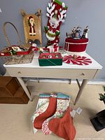 Overall lot on table and floor showing baskets, stockings, plaques, trivets, mug and other items
