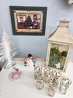 Group shot of all items on table including framed print, metal tree, six glasses, lantern, large ornament, ceramic snowman