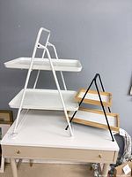 White metal two-tier folding display stand and black metal/wood two-tier stand on tabletop