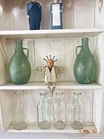 Full view of two green glass jugs, wooden angel, four milk bottles, two carved figurines
