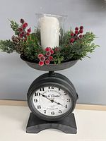 Front view of scale shaped clock with holiday greenery, glass hurricane and candle