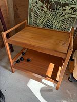 Full view of teak cart showing two shelves and loose caster wheels on lower shelf