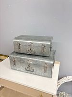 Two galvanized metal suitcases stacked showing front latches and overall appearance
