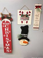 Four wooden Christmas wall hangings displayed vertically on wall