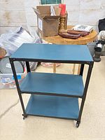 Front view showing three blue wooden shelves and metal frame on casters