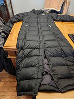 Full view of The North Face long black puffer coat laid flat