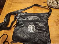 Front view small black shoulder bag with medallion and multiple zippers