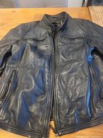 Front view of black Danier leather moto jacket laid flat showing zipper, chest pockets and hand pockets