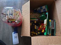 Cardboard box containing assorted LEGO pieces beside off-brand snow globe