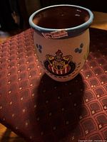 Cup upright showing crest design, blue rim, brown interior