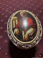 Top view of porcelain trinket box showing portrait and gilt/red cabochon border