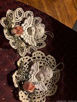 Front view of both cherub ornaments showing faces, wings, crochet backings and silk flowers