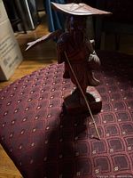 Front view of wooden figurine standing with bamboo stick