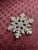 Front view of the glittered plastic snowflake ornament on patterned fabric