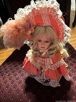 Front view of porcelain doll in coral Victorian dress and bonnet, seated