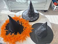 Three sample witch hats: spider print, plain black, orange-feather trim