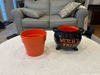 Front view of orange planter and black Witch's Brew cauldron bowl